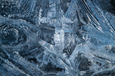 Kum dalgalarının yakın plan görüntüsü, buz tozu ile birlikte, desenli ve dalgalı bir desen oluşturur. Koyu kum ve buzlu mavi tonlar arasındaki zıtlık doğal oluşumları vurgular..