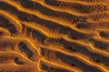 Sıcak güneş ışığıyla aydınlatılan desenli kum dalgalarının yakın çekimi çarpıcı bir ışık ve gölge deseni yaratıyor. Doğal oluşumlar rüzgar şeklindeki manzaraların güzelliğini vurgular..