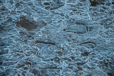 Parçalanmış buza yakın çekim ve karmaşık kristal desenler. Donmuş yüzey ışığın altında parlıyor ve kırılan buz oluşumlarının büyüleyici bir dokusunu oluşturuyor..