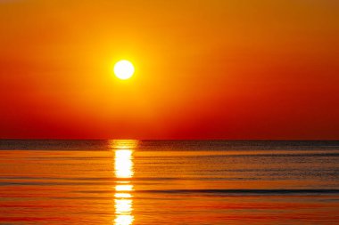 Okyanus üzerinde büyüleyici bir günbatımı, gökyüzü ve su boyunca altın ve turuncu renkler döküyor. Güneşin yansıması huzurlu ve sıcak bir atmosfer yaratır..