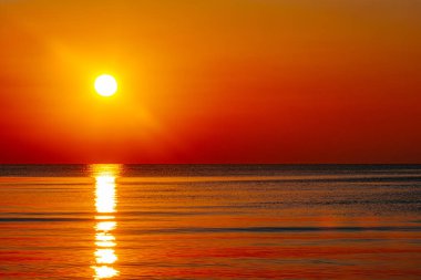 Okyanus üzerinde büyüleyici bir günbatımı, gökyüzü ve su boyunca altın ve turuncu renkler döküyor. Güneşin yansıması huzurlu ve sıcak bir atmosfer yaratır..