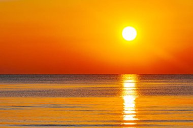 Okyanus üzerinde büyüleyici bir günbatımı, gökyüzü ve su boyunca altın ve turuncu renkler döküyor. Güneşin yansıması huzurlu ve sıcak bir atmosfer yaratır..