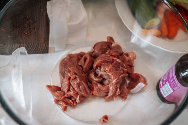 Mutfak masasında çiğ et, erişte, sos ve sebzelerin yanı sıra yemek hazırlığı için hazırlanmış tahta ve bıçaklar bulunuyor. 02.16.2025 Brenguli, Letonya