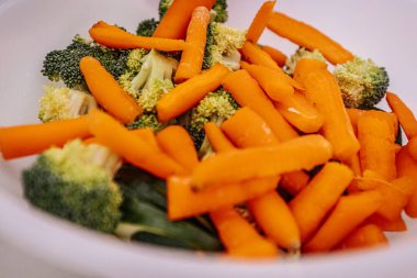 Taze doğranmış havuç, brokoli ve bambu filizleriyle dolu bir kasenin yakın çekimi. Canlı turuncu ve yeşil renkler taze malzemelerin altını çiziyor, pişirmeye ya da servis etmeye hazır..