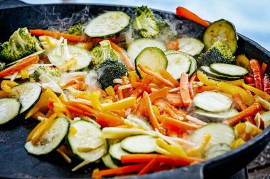 A steaming vegetable stir-fry with zucchini, bell peppers, carrots, and broccoli is being cooked in a pan. A spatula is stirring the fresh, colorful ingredients. clipart