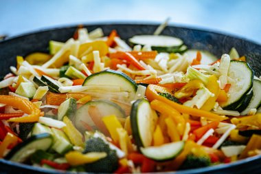 Kabaklı, dolgun biberli, havuçlu ve brokolili dumanı tüten sebze kızartması bir tavada pişiriliyor. Bir spatula taze, renkli malzemeleri karıştırıyor..