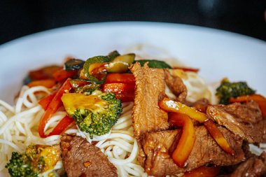 Kırmızı dolmalık biber, brokoli ve kabak da dahil olmak üzere sebzeli ızgara sığır eti. Lezzetli bir sosta erişteyle servis ediliyor. Lezzetli ve renkli bir Asya yemeği..