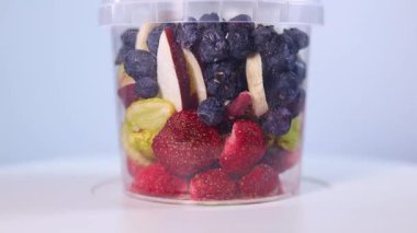 A transparent jar filled with a colorful assortment of freeze-dried fruits and vegetables, including blueberries, cranberries, raspberries, apple slices, pumpkin cubes, and more.