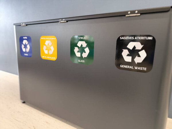 A four-section recycling bin with color-coded labels for paper, metal and plastic, glass, and general waste. Designed for efficient waste sorting in an indoor space. Eco-friendly solution.