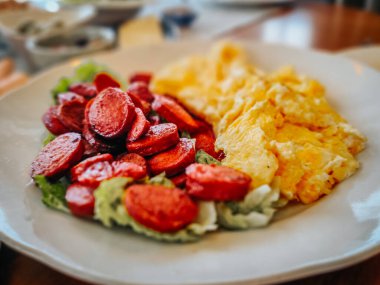 Yağda yumurta, kızarmış sosis dilimleri ve dengeli ve lezzetli bir sabah yemeği için taze marul içeren doyurucu bir kahvaltı tabağı.