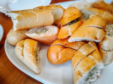 Bir tabak dilimlenmiş sarımsaklı ekmek. İçi tereyağı dolu. Altın kabuğu ve yumuşak iç yüzüyle sergileniyor. Lezzetli bir aperatif veya her yemek için mükemmel bir meze..