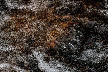 Hızlı akan bir derenin yüzeyinde köpüklü baloncukların detaylı bir yakın çekimi. Karmaşık doku ve yansımalar doğadaki suyun dinamik hareketini yakalar..