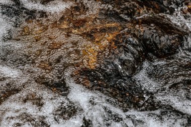 Hızlı akan bir derenin yüzeyinde köpüklü baloncukların detaylı bir yakın çekimi. Karmaşık doku ve yansımalar doğadaki suyun dinamik hareketini yakalar..