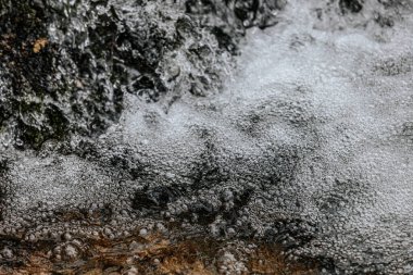 Hızlı akan bir derenin yüzeyinde köpüklü baloncukların detaylı bir yakın çekimi. Karmaşık doku ve yansımalar doğadaki suyun dinamik hareketini yakalar..