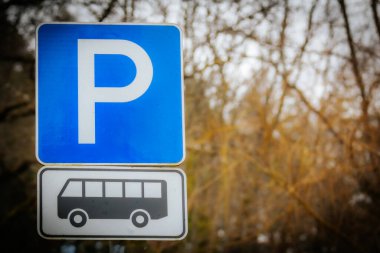 Otobüs parkı işareti olan mavi bir park levhası. Arka planda bulanık ağaç dalları var, doğal bir açık hava ortamı yaratıyor..