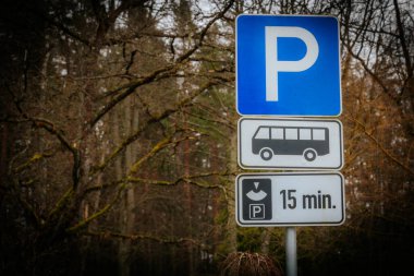 Otobüs parkı işareti olan mavi bir park levhası. Arka planda bulanık ağaç dalları var, doğal bir açık hava ortamı yaratıyor..