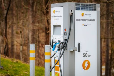 Bir Elektrum Drive elektrikli araç şarj istasyonu çoklu şarj bağlantıları açık havada kurulur. Letonya metni EV şarjı olduğunu gösteriyor..