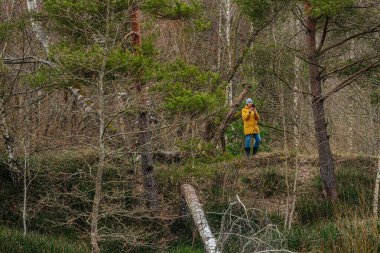 Siyah kışlık ceket giyen, kızıl saçlı ve gözlüklü yaşlı bir kadının portresi. Ciddi ifadesi bulanık orman geçmişiyle çelişiyor. Doğal ve düşünceli bir atmosfer yaratıyor..