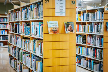 Renkli kitaplarla dolu düzgün düzenlenmiş kitaplıkları olan iyi ışıklandırılmış bir kütüphane. Modern iç mekan okuma, araştırma ve araştırma için davet edici bir alan yaratır. 08.03.2025 Valmiera, Letonya