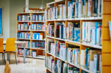  Kitaplıklarla dolu parlak ve modern bir kütüphane ve renkli yayınların sergilendiği dönen bir sergi rafı. İyi organize edilmiş alan okumayı davet ediyor. 08.03.2025 Valmiera, Letonya