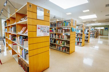 Renkli kitaplarla dolu düzgün düzenlenmiş kitaplıkları olan iyi ışıklandırılmış bir kütüphane. Modern iç mekan okuma, araştırma ve araştırma için davet edici bir alan yaratır. 08.03.2025 Valmiera, Letonya