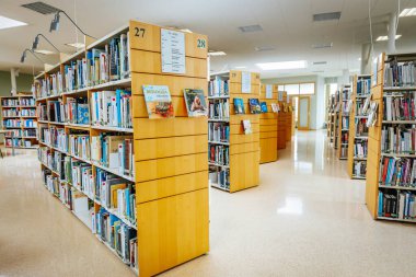 Renkli kitaplarla dolu düzgün düzenlenmiş kitaplıkları olan iyi ışıklandırılmış bir kütüphane. Modern iç mekan okuma, araştırma ve araştırma için davet edici bir alan yaratır. 08.03.2025 Valmiera, Letonya