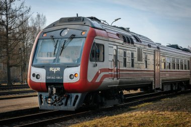 Sessiz bir tren istasyonunda bir kişi kırmızı ve gümüş bir trene biner. Tren Rga 'ya gidecek ve platform sokak lambalarıyla dolu. 03.08.2025 Valmiera, Letonya