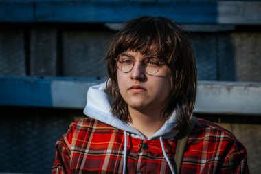  Ekose ceketli ve gözlüklü genç adam güneş ışığında güneşlenirken gözleri kapalı oturuyor. Onların barışçıl ifadeleri bir açık hava ortamında rahatlama, içgözlem ve farkındalık taşır..