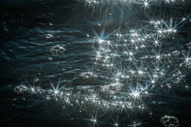 Güneş ışığı dalgalanan sudan yansıyarak büyüleyici bir yıldız patlaması etkisi yaratır. Parlak, kesişen ışık ışınları su yüzeyinde rüya gibi ve soyut bir desen oluşturur..