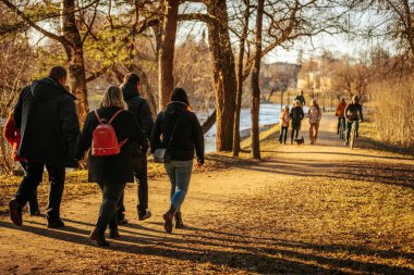 İnsanlar parkta güneşli bir günün tadını çıkarıyorlar. Ağaçlarla kaplı manzaralı bir patika boyunca bisiklet sürüp yürüyorlar. Sıcak güneş ışığı açık hava atmosferini canlandırır. 03.09.2025 Valmiera, Letonya
