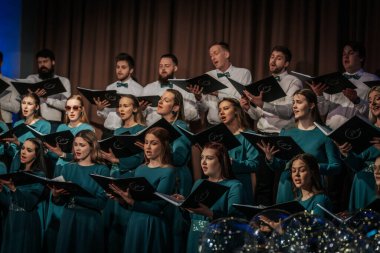 Bir orkestra şefinin yönetiminde sahnedeki canlı performansları senkronize ve tutkulu bir şekilde müzik kağıtları tutan bir koro şefinin yönetiminde sahneye çıkıyor. 03.15.2025 Valmiera, Letonya