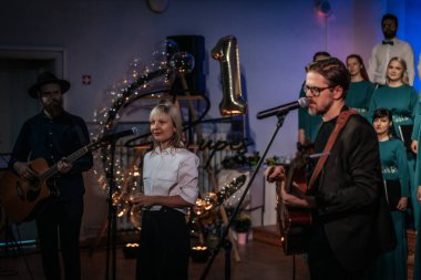 Bir orkestra şefinin yönetiminde sahnedeki canlı performansları senkronize ve tutkulu bir şekilde müzik kağıtları tutan bir koro şefinin yönetiminde sahneye çıkıyor. 03.15.2025 Valmiera, Letonya