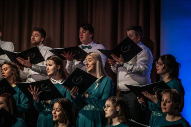 Bir orkestra şefinin yönetiminde sahnedeki canlı performansları senkronize ve tutkulu bir şekilde müzik kağıtları tutan bir koro şefinin yönetiminde sahneye çıkıyor. 03.15.2025 Valmiera, Letonya
