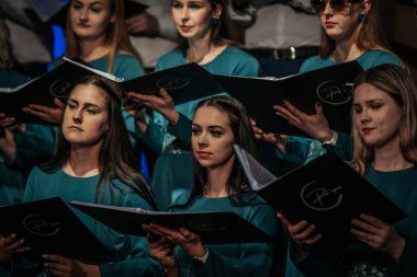 Bir orkestra şefinin yönetiminde sahnedeki canlı performansları senkronize ve tutkulu bir şekilde müzik kağıtları tutan bir koro şefinin yönetiminde sahneye çıkıyor. 03.15.2025 Valmiera, Letonya
