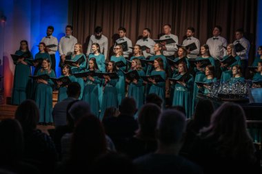 Bir orkestra şefinin yönetiminde sahnedeki canlı performansları senkronize ve tutkulu bir şekilde müzik kağıtları tutan bir koro şefinin yönetiminde sahneye çıkıyor. 03.15.2025 Valmiera, Letonya