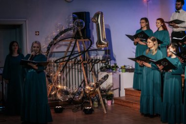 Bir orkestra şefinin yönetiminde sahnedeki canlı performansları senkronize ve tutkulu bir şekilde müzik kağıtları tutan bir koro şefinin yönetiminde sahneye çıkıyor. 03.15.2025 Valmiera, Letonya