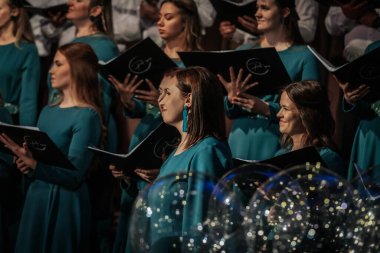 Bir orkestra şefinin yönetiminde sahnedeki canlı performansları senkronize ve tutkulu bir şekilde müzik kağıtları tutan bir koro şefinin yönetiminde sahneye çıkıyor. 03.15.2025 Valmiera, Letonya