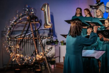 Bir orkestra şefinin yönetiminde sahnedeki canlı performansları senkronize ve tutkulu bir şekilde müzik kağıtları tutan bir koro şefinin yönetiminde sahneye çıkıyor. 03.15.2025 Valmiera, Letonya