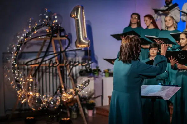 Bir orkestra şefinin yönetiminde sahnedeki canlı performansları senkronize ve tutkulu bir şekilde müzik kağıtları tutan bir koro şefinin yönetiminde sahneye çıkıyor. 03.15.2025 Valmiera, Letonya