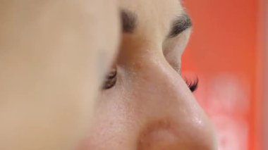 A close-up of a woman applying makeup with a brush, highlighting her flawless skin, long eyelashes, and well-defined eyebrows. The beauty routine takes place in a cosmetic setting.sstk Diverse Beauty