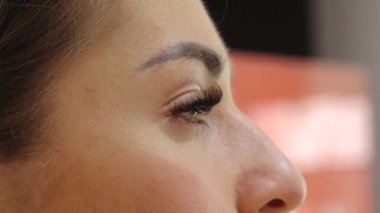 A close-up of a woman applying makeup with a brush, highlighting her flawless skin, long eyelashes, and well-defined eyebrows. The beauty routine takes place in a cosmetic setting.sstk Diverse Beauty