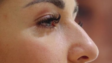 A close-up of a woman applying makeup with a brush, highlighting her flawless skin, long eyelashes, and well-defined eyebrows. The beauty routine takes place in a cosmetic setting.sstk Diverse Beauty