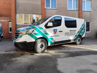 Yeşil ve beyaz işaretli bir Letonya belediye polis minibüsü eski tuğla binaların yanındaki kaldırım taşı bir sokakta park halinde. Pasvaldibas Policija metni. 03.19.2025 Limbazi, Letonya