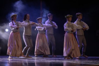 22.03.2025 Limbazi, Letonya. Letonyalı gençlerin dans gösterisi. Limbazi Kültür Merkezi. Halk dansçıları sahnede geleneksel Letonya kıyafetleriyle, çizgili etekler, yeleklerle ve çiçek taçlarıyla gösteri yapıyorlar..