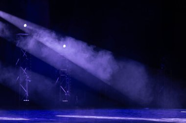 Mor sahne ışıkları sisli sisi delip geçer, karanlık bir tiyatro ortamında metal kirişleri vurgular. Güçlü atmosfer ve aydınlatma efektleri.