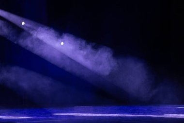 Mor sahne ışıkları sisli sisi delip geçer, karanlık bir tiyatro ortamında metal kirişleri vurgular. Güçlü atmosfer ve aydınlatma efektleri.