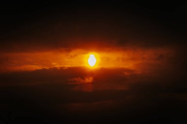 Kısmi güneş tutulması dramatik kırmızı-turuncu bulutlar arasında parlayarak karanlık bir gökyüzünde yoğun ve gerçeküstü bir ışık oluşturur. Çoklu kopyalama alanı içerir.