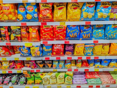 Açık fiyatlı süpermarket raflarında Lays ve Dau da dahil olmak üzere çeşitli markalardan çeşitli patates cipsleri ve abur cuburlar. 03.27.2025 Valmiera, Letonya