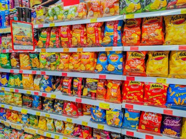 Açık fiyatlı süpermarket raflarında Lays ve Dau da dahil olmak üzere çeşitli markalardan çeşitli patates cipsleri ve abur cuburlar. 03.27.2025 Valmiera, Letonya