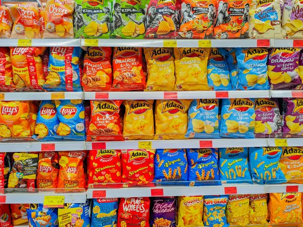 Açık fiyatlı süpermarket raflarında Lays ve Dau da dahil olmak üzere çeşitli markalardan çeşitli patates cipsleri ve abur cuburlar. 03.27.2025 Valmiera, Letonya